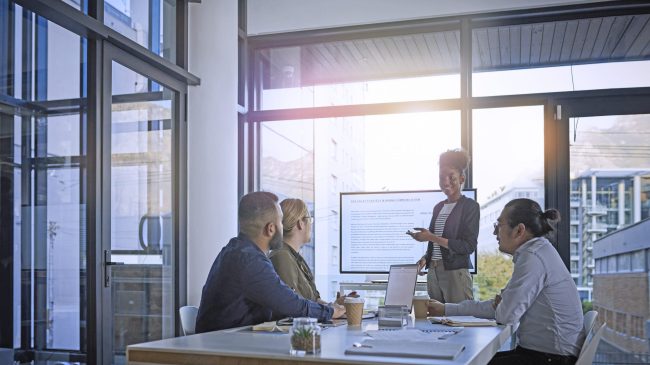 Business people in a meeting where a lady stands in front of the group presenting